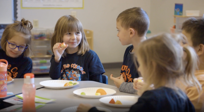 Girl holding fruit talking smiling at boy during 4K snack time