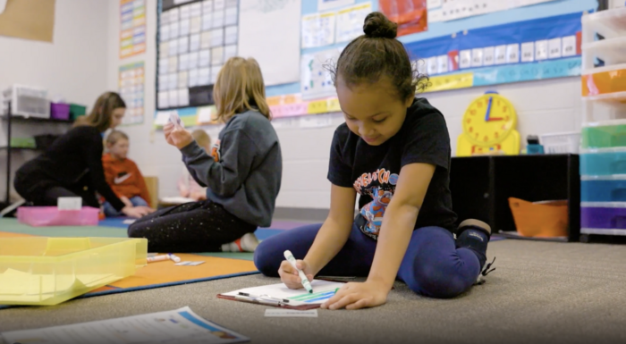 Girl coloring on worksheet on carpeted floor